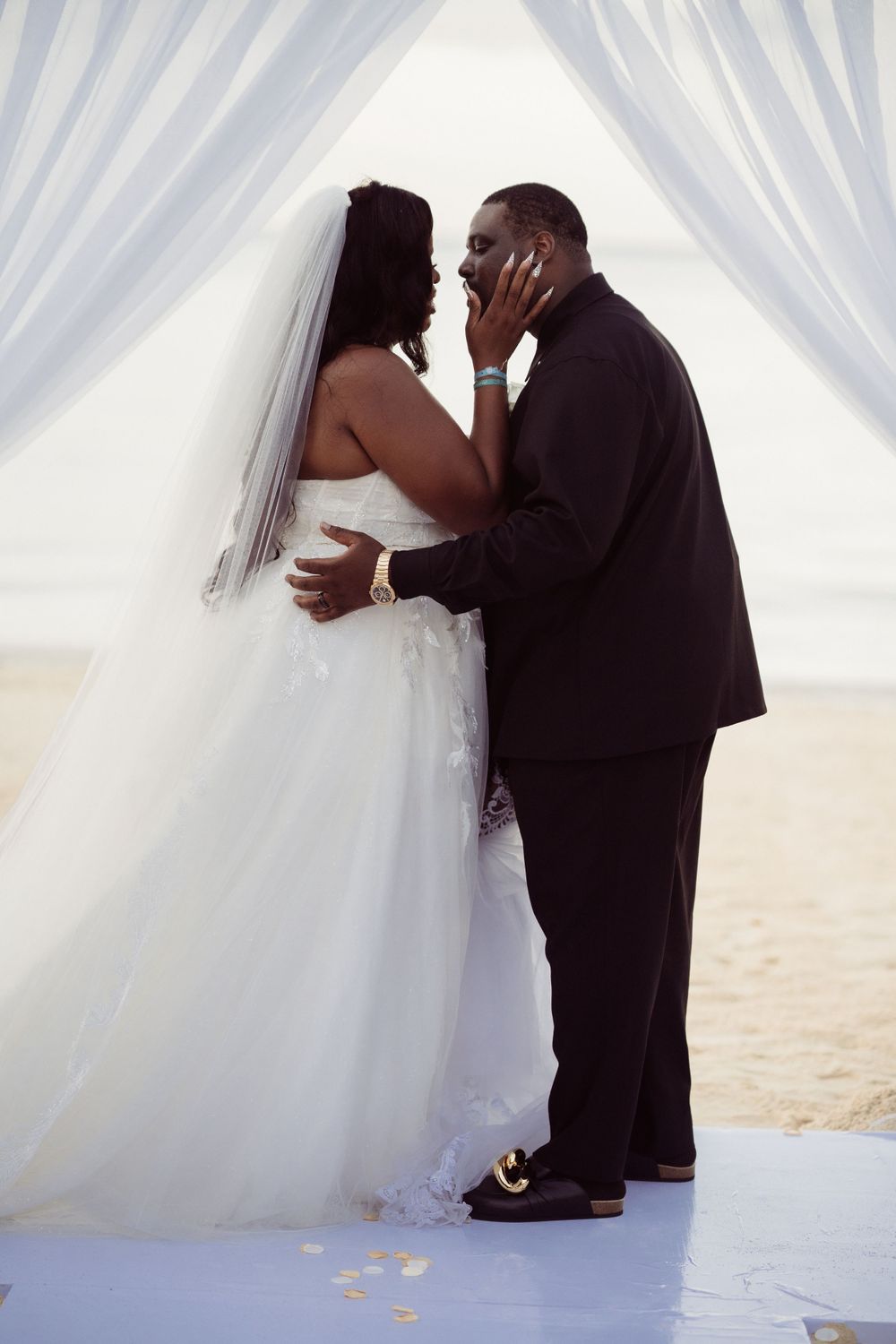 A touching moment between newlyweds under white drapes at a beach wedding ceremony.