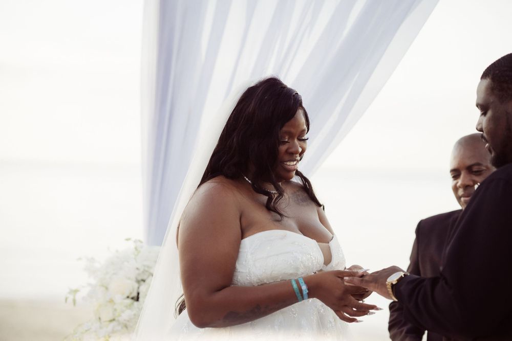 A joyful bride smiling during her beach wedding ceremony as she exchanges rings.