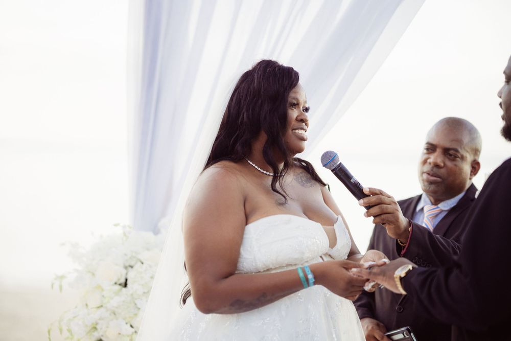 A radiant bride laughs during her beach wedding ceremony while exchanging vows.