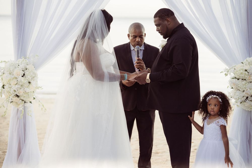 An intimate beach wedding ceremony with white floral arrangements and flowing curtains.