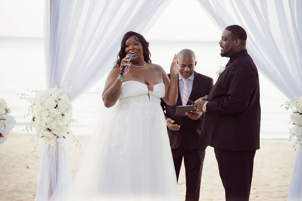 An emotional moment during a beach wedding ceremony as the bride speaks under white drapes.