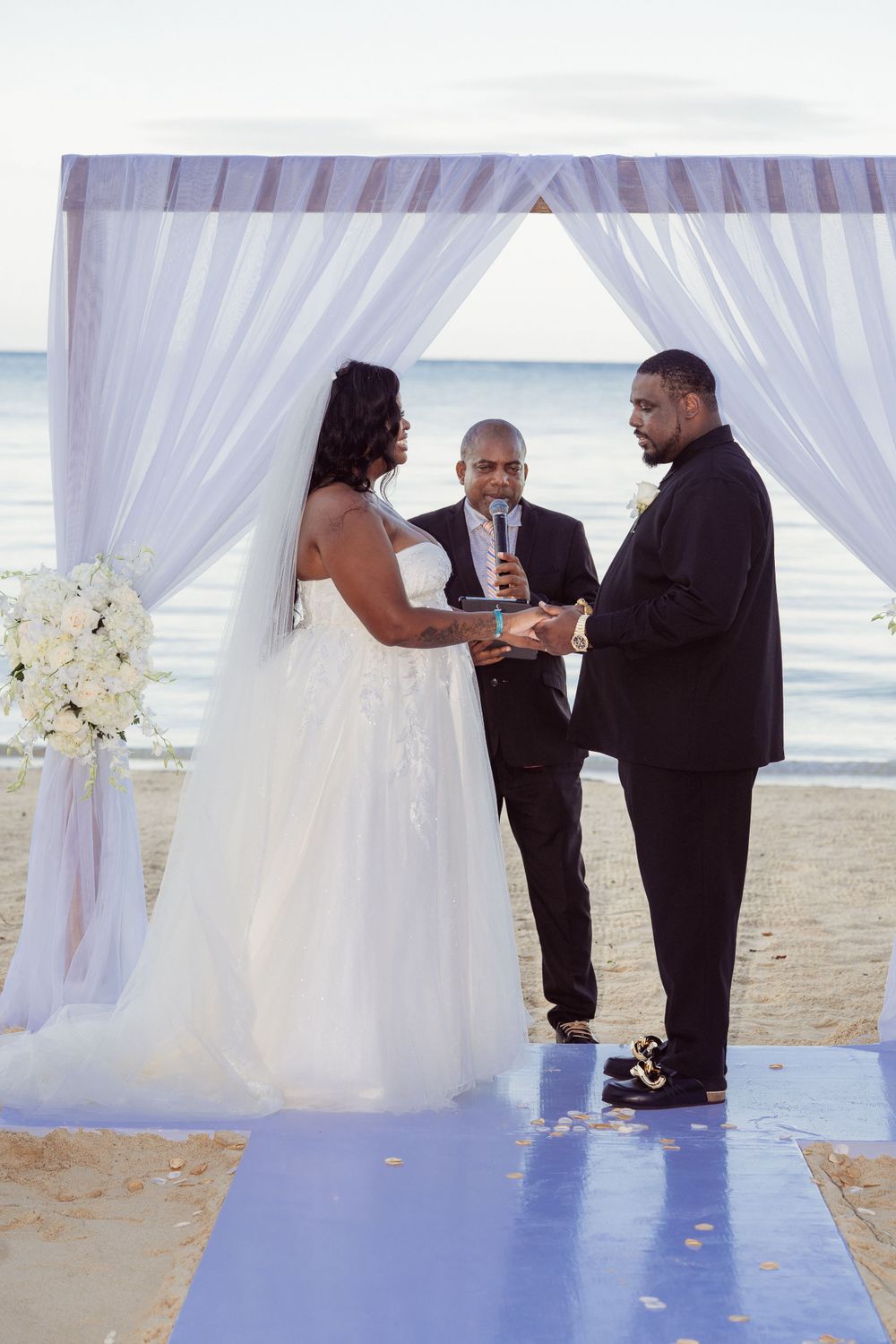 A beachside wedding ceremony under white drapes with floral arrangements and ocean backdrop.