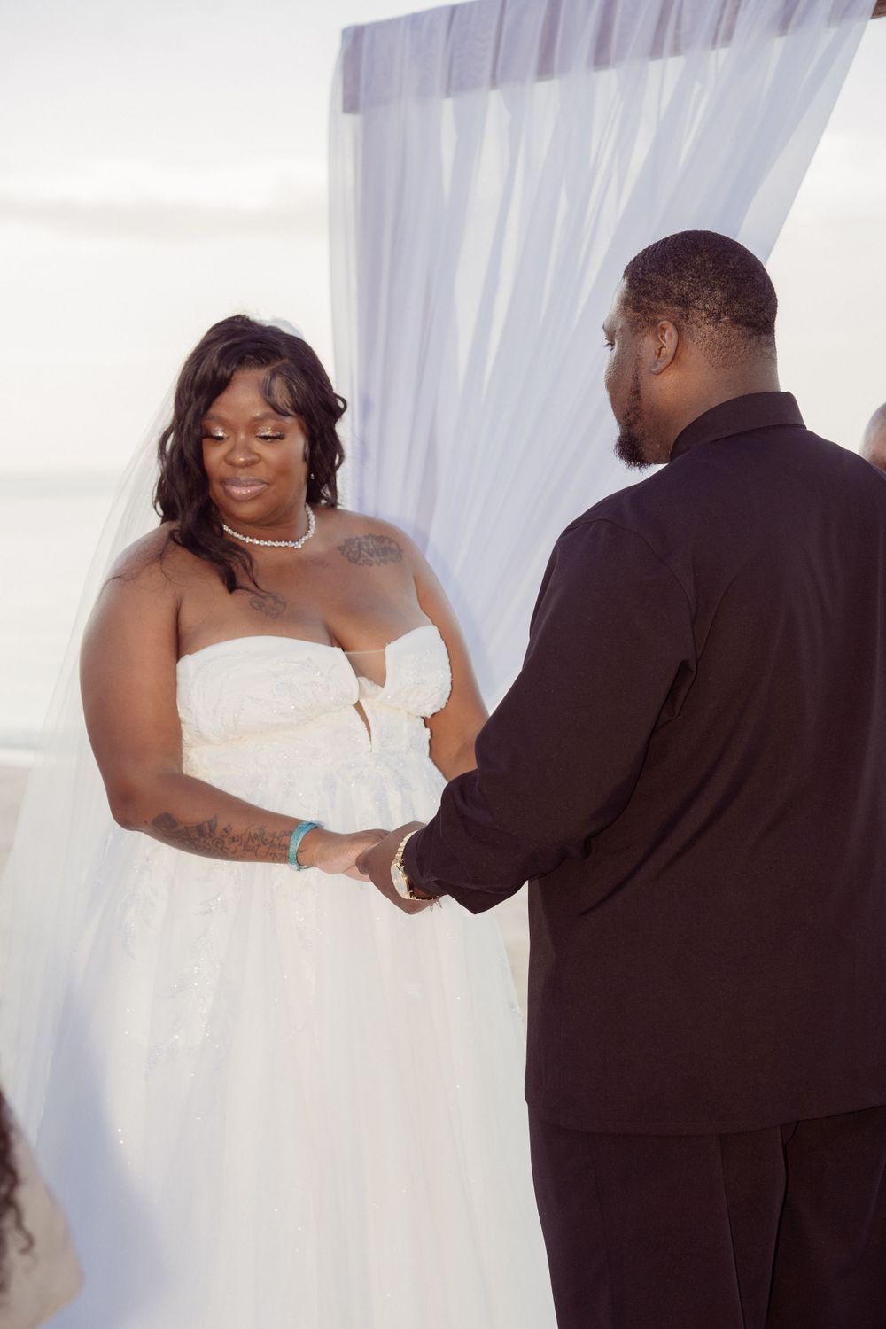 A tender moment between a couple exchanging vows during their wedding ceremony in front of a white curtain backdrop.