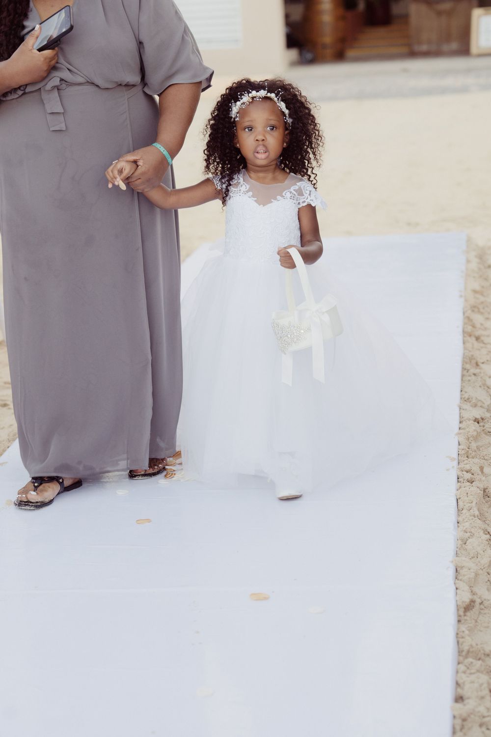 Young flower girl in white dress holding a bouquet walking down the aisle on a white carpet.