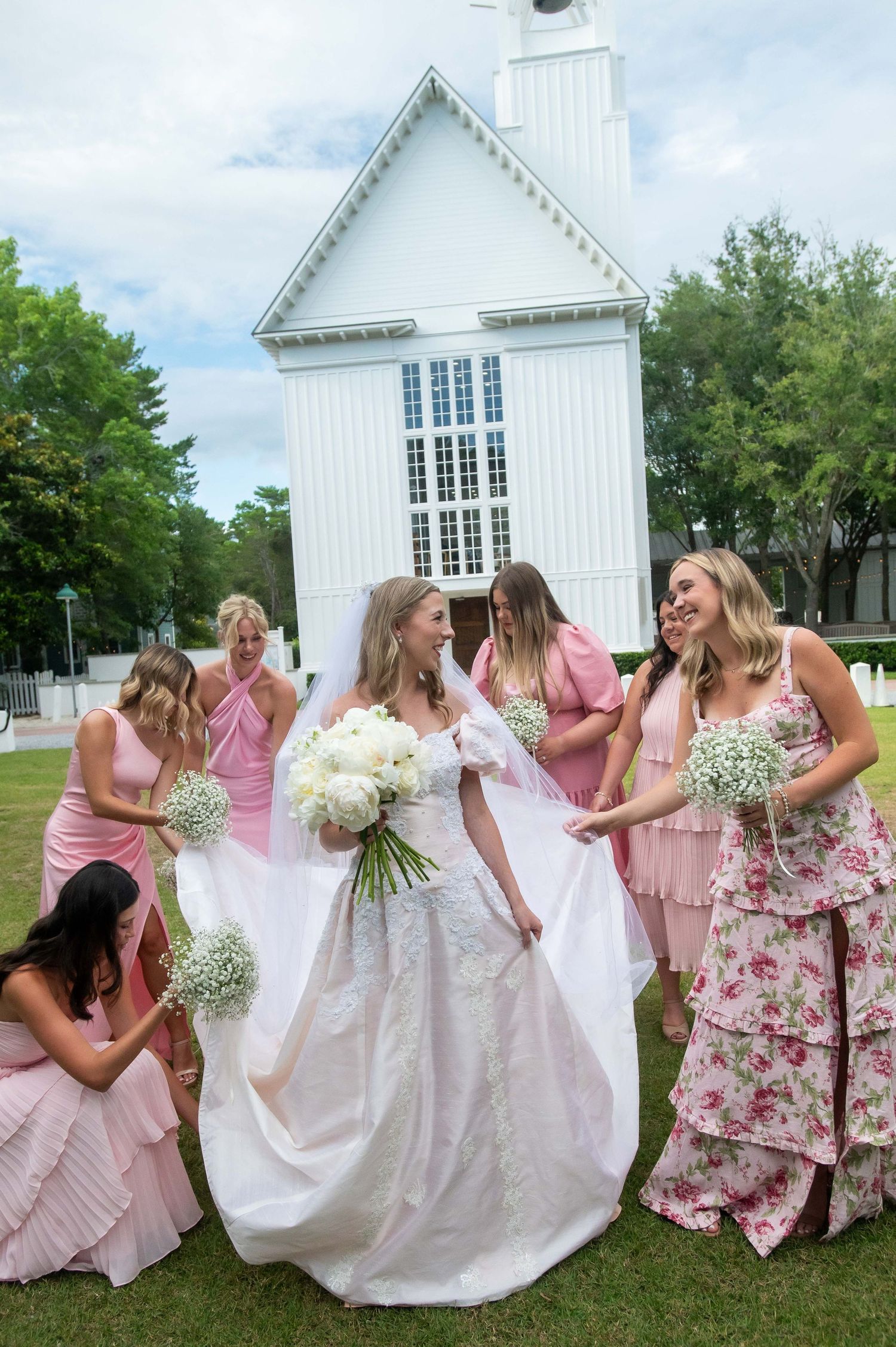 A group in pink dresses and a white gown poses playfully in a sequence of photos in front of a white chapel.