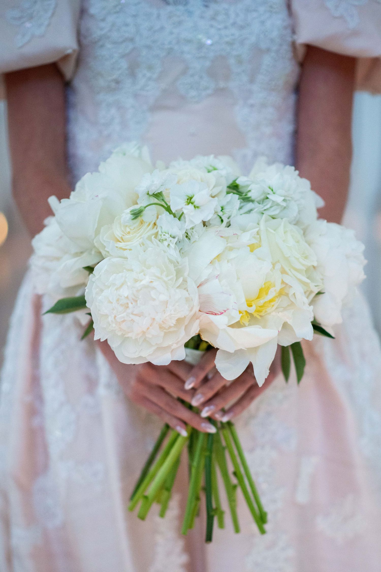 Close-up view of three elegant white peony bouquets held against blush pink bridesmaid dresses.