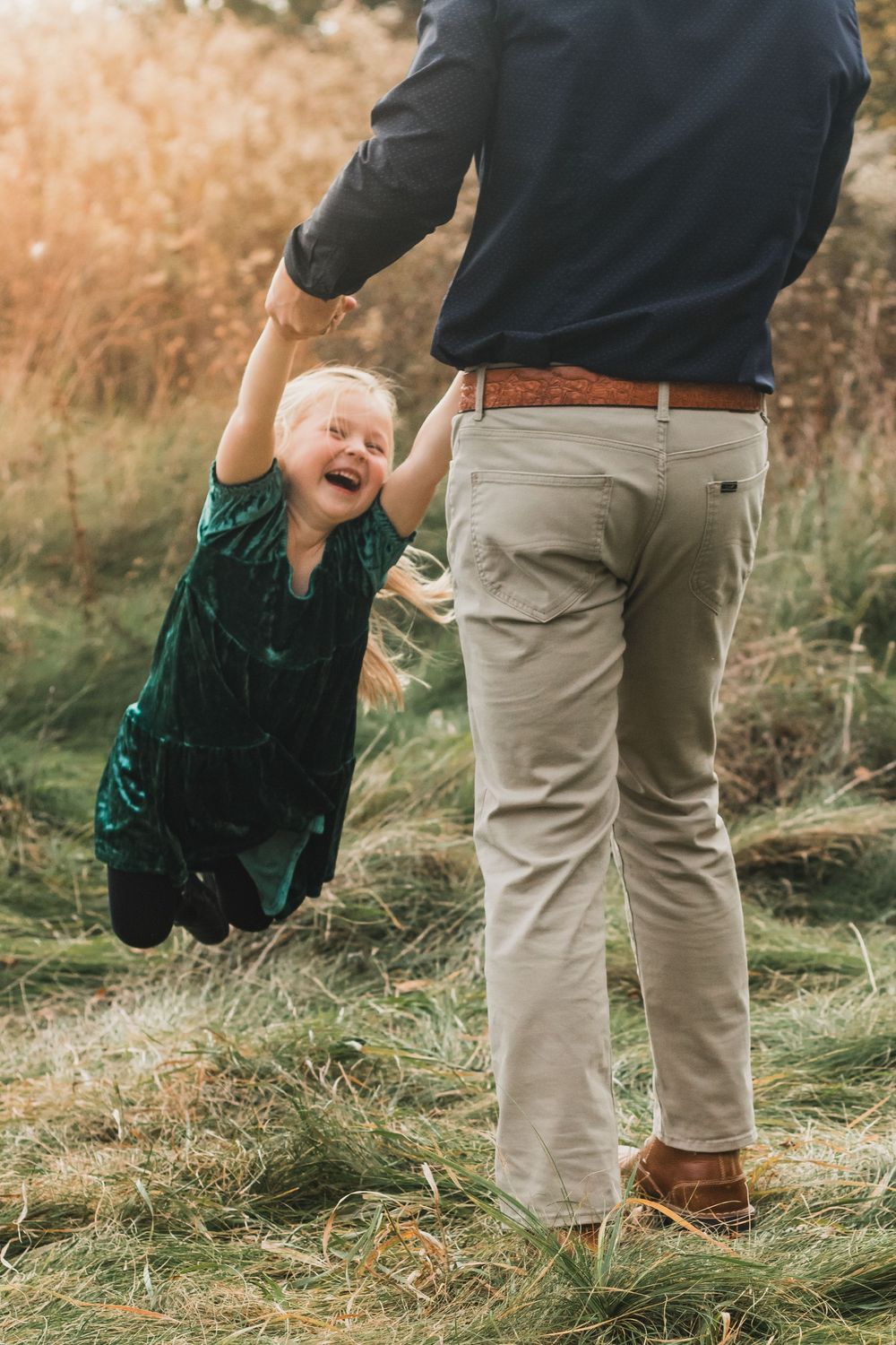 Father swinging his daughter around during a golden hour lifestyle family photo session in Farmington Hills, Michigan.