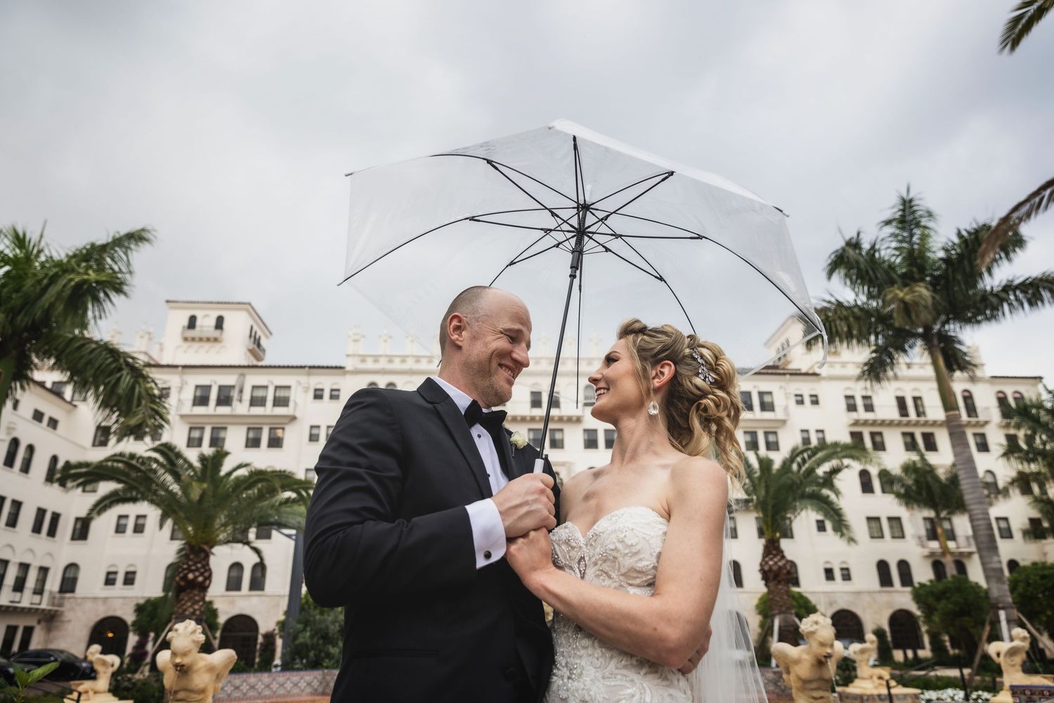 A couple shares an intimate moment during their wedding celebration at a Mediterranean-style venue with palm trees.