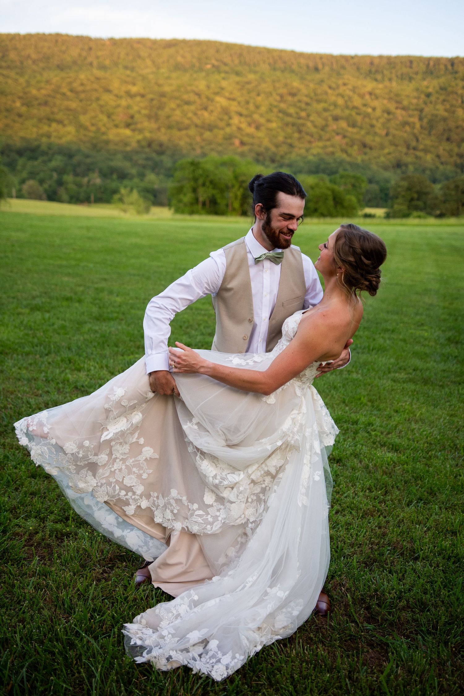 A romantic couple dances in a grassy field with an autumn mountain landscape in the background during their wedding day.