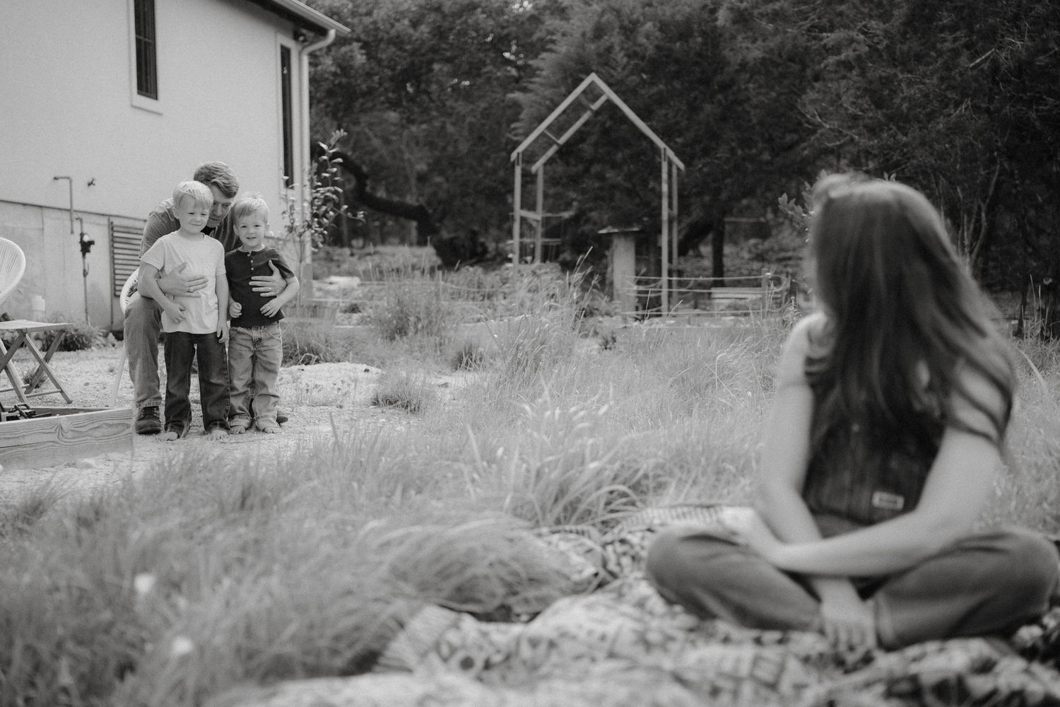 A black and white photograph showing people gathered in an overgrown garden near a small structure.