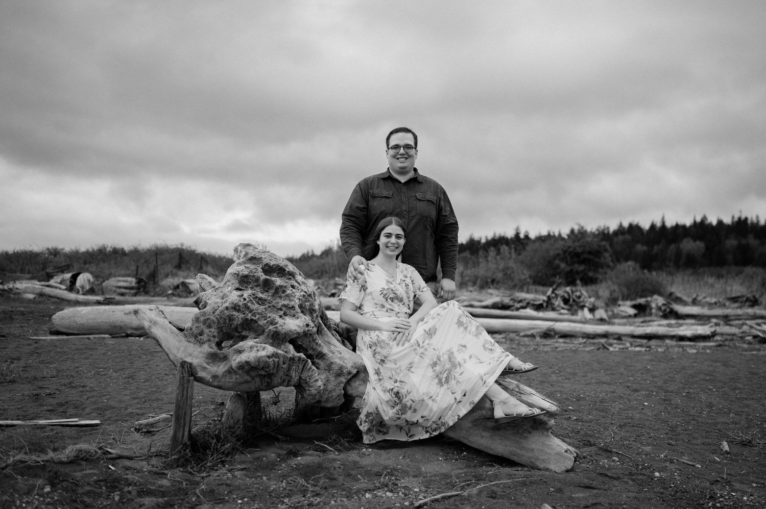 A black and white photo of two people sitting on driftwood at a Pacific Northwest beach.