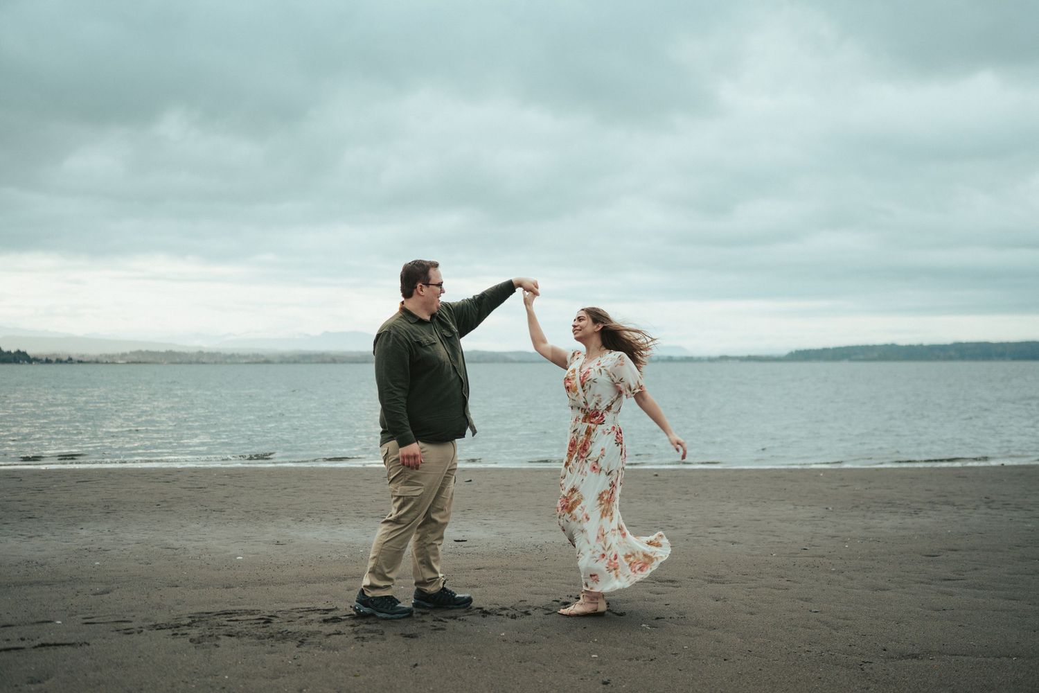 A couple dancing and twirling together on a misty beach with water in the background.
