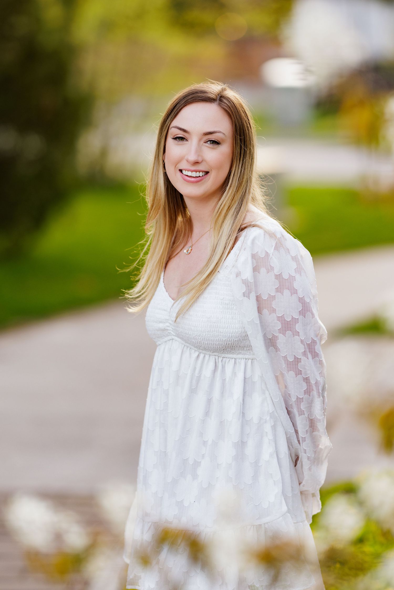 Person wearing a white lace dress with long sleeves standing outdoors on a pathway in natural lighting.