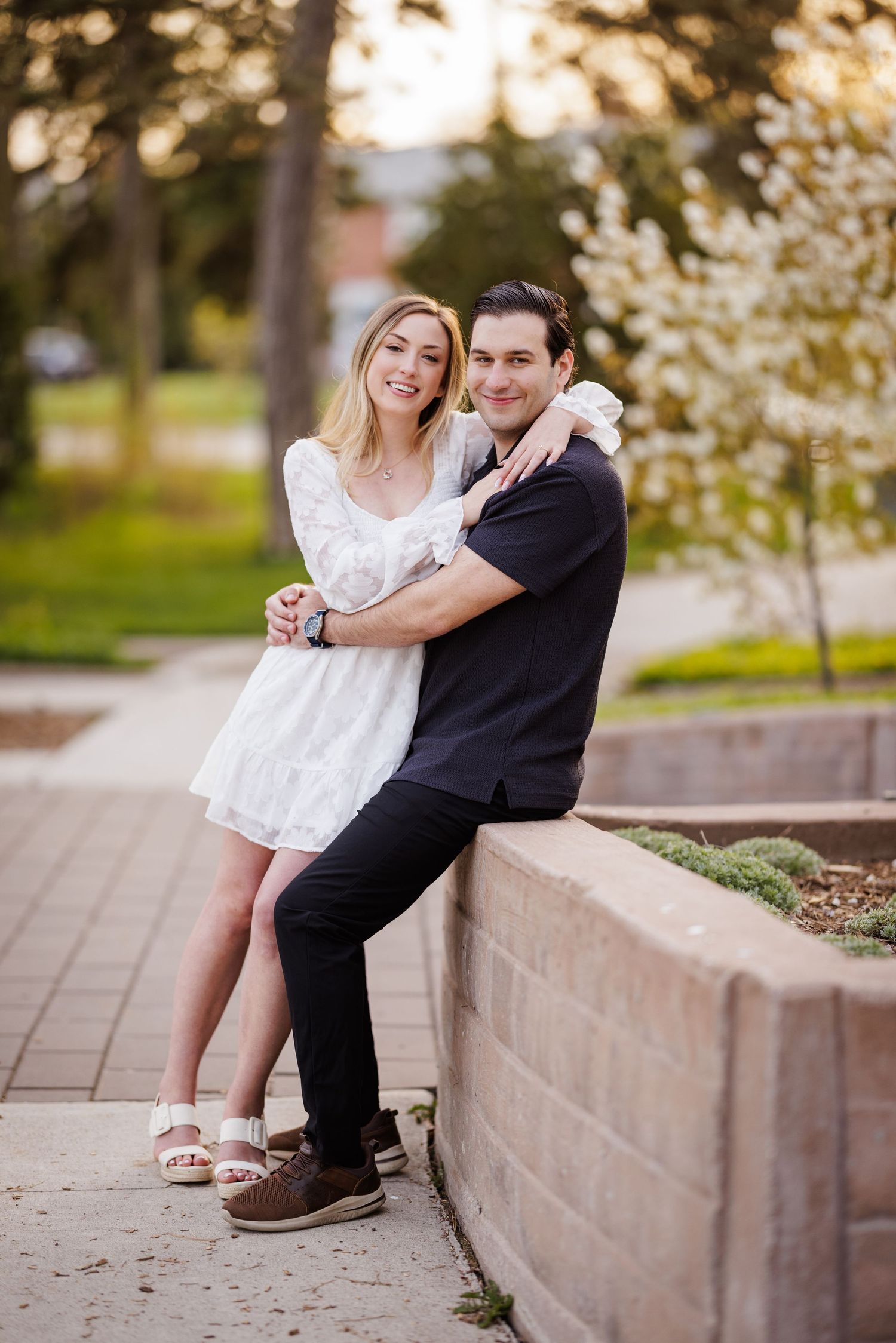 Couple sitting and cuddling on stone wall during outdoor photoshoot.
