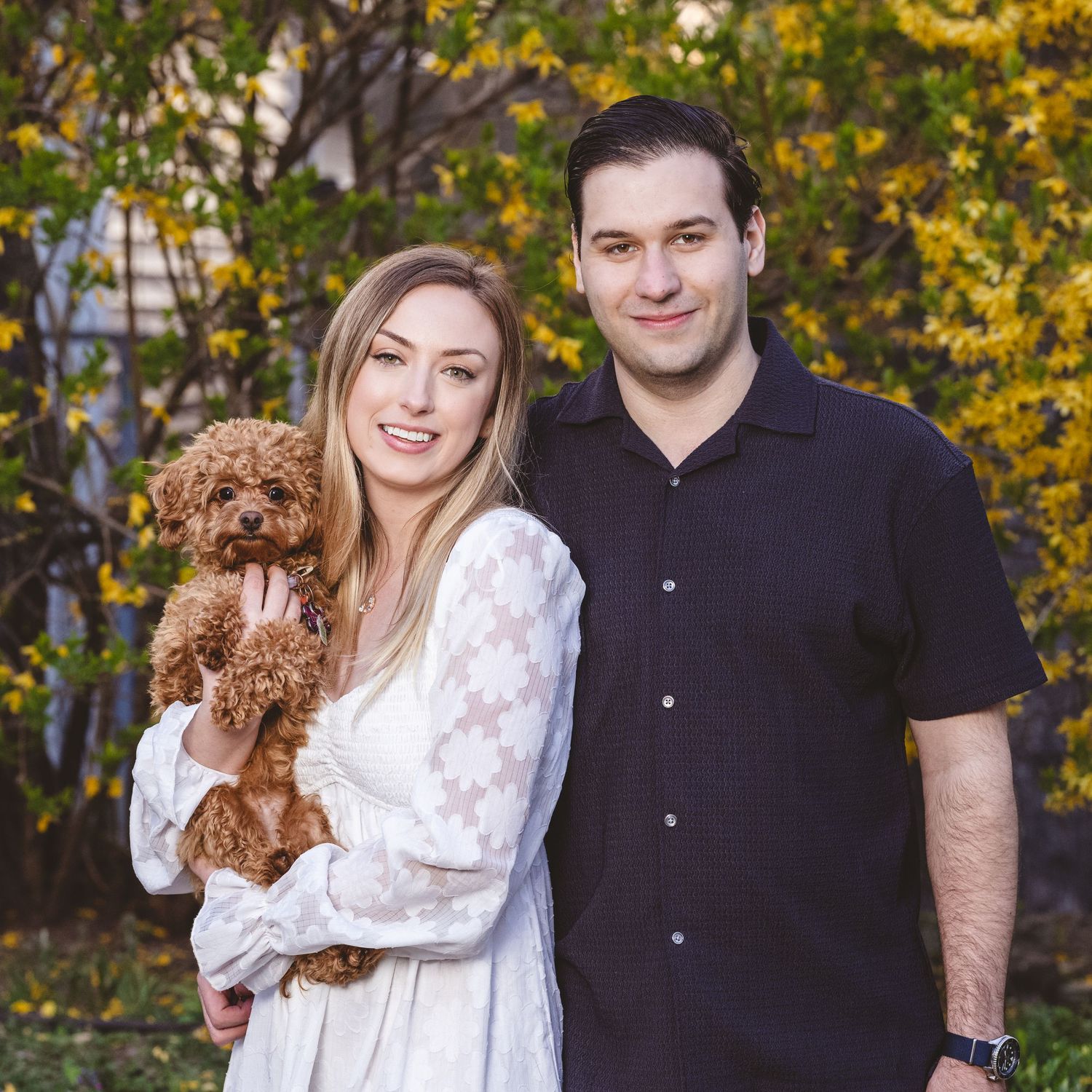Autumn photoshoot outdoors in a park with people and a small brown dog against colorful fall foliage.
