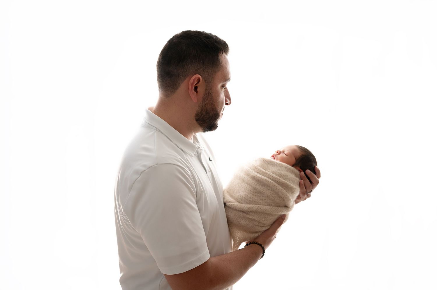 Person in white shirt holding swaddled newborn against white background.