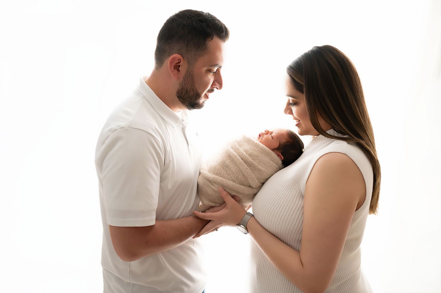 Family members share tender moments while holding a newborn baby against a white background.