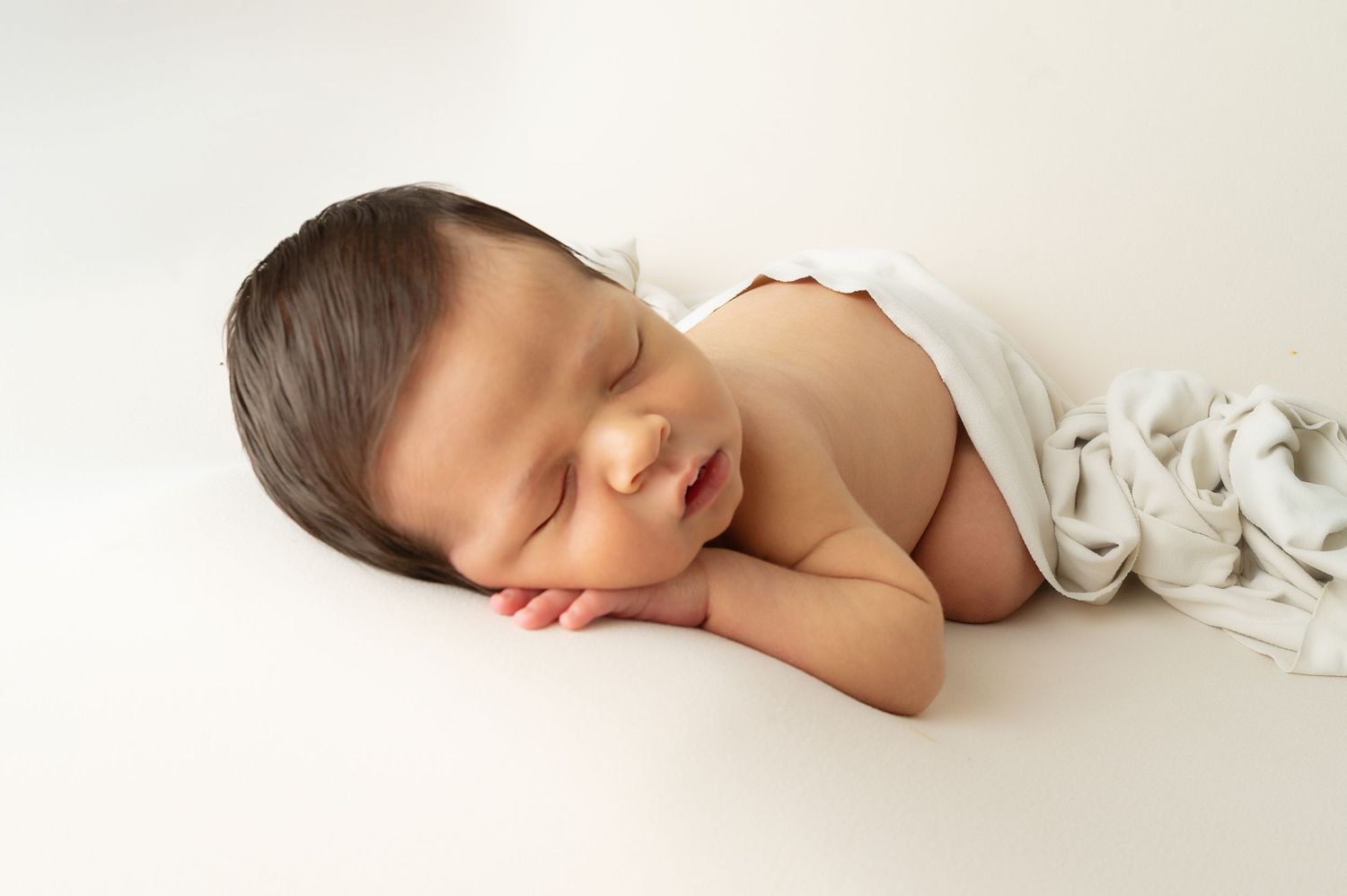Peaceful sleeping newborn lying on white background during portrait session.