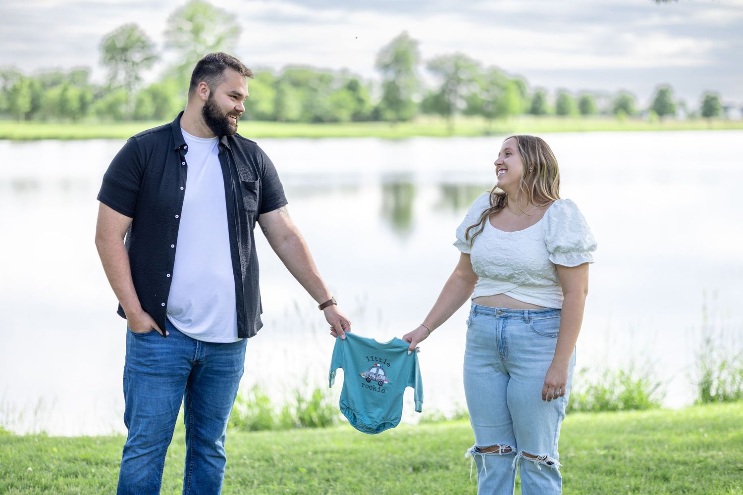 Springfield, IL photographer captures a couple holding a onesie that says "Little Rookie" during a session in Central, IL