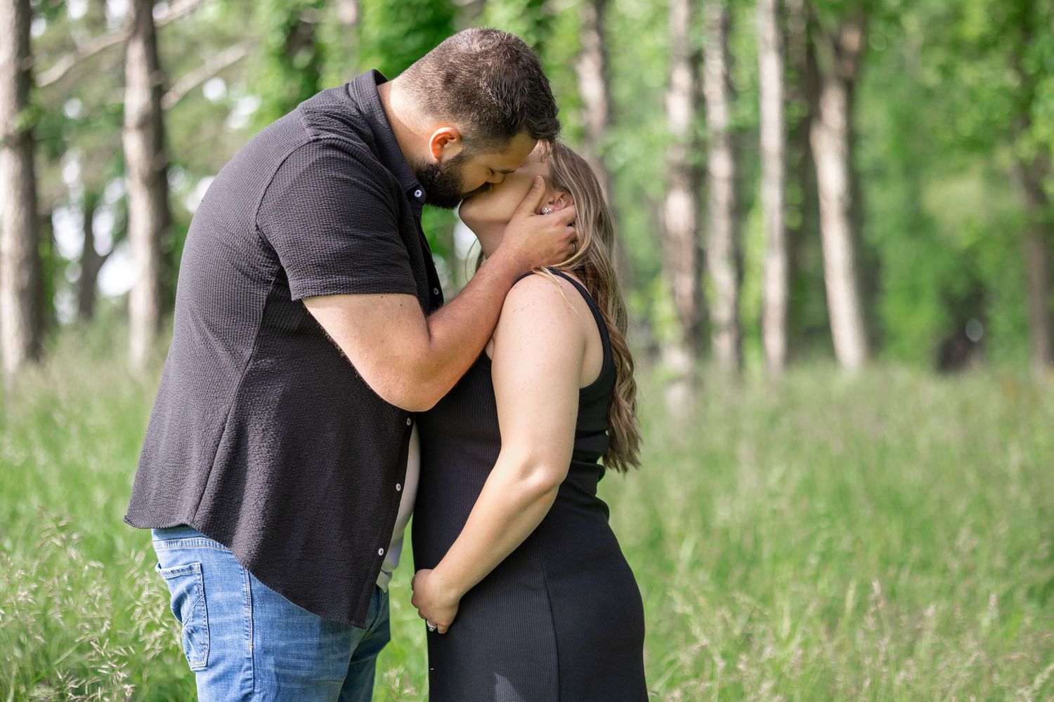 Springfield, IL photographer captures a couple kissing in tall grass while holding their expecting baby during a session in Central, IL