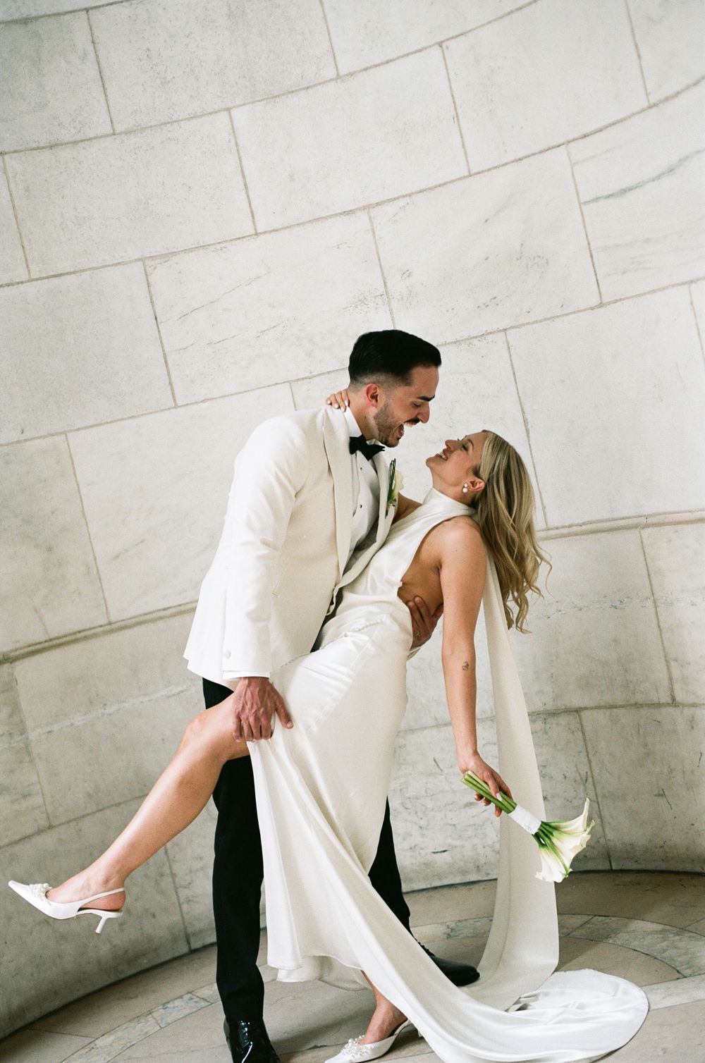 A romantic couple in matching white outfits share a tender dance moment against a light-colored wall. paris editorial wedding photographer,
