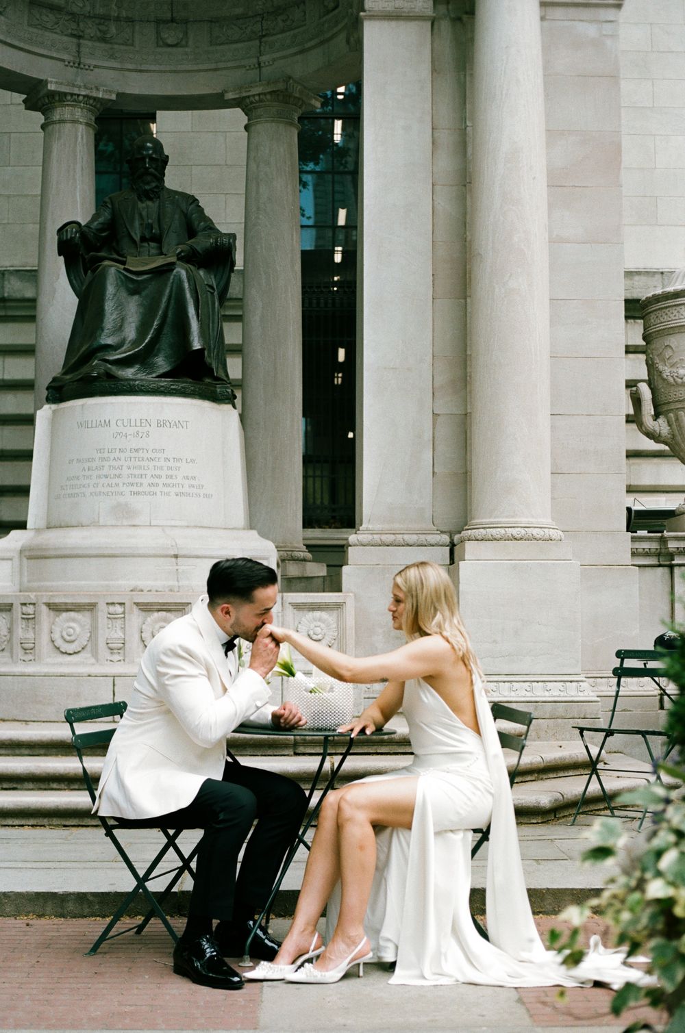 Romantic couple in white outfits sitting on stone steps of neoclassical building with columns. paris film photography, paris wedding photos