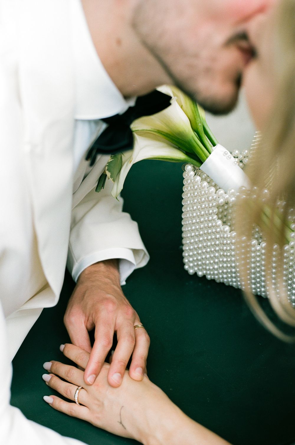 Close-up of hands wearing wedding rings with white calla lily boutonniere against emerald green background. paris wedding photography