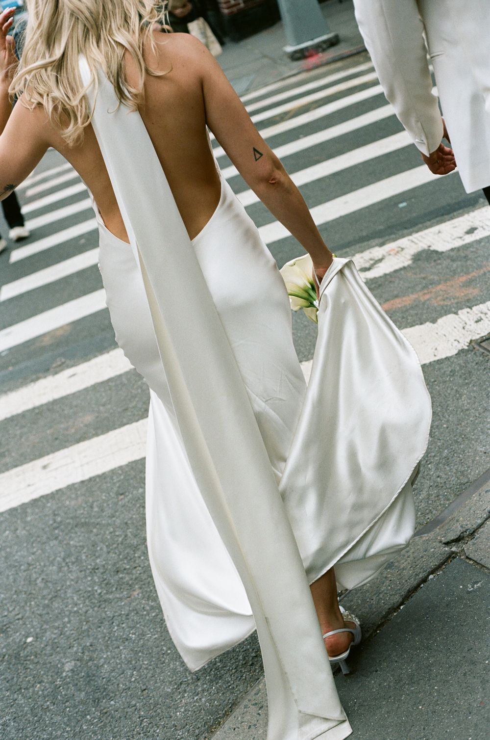 Flowing white backless maxi dress billows elegantly as someone crosses a street with zebra crossings. editorial paris wedding, paris film