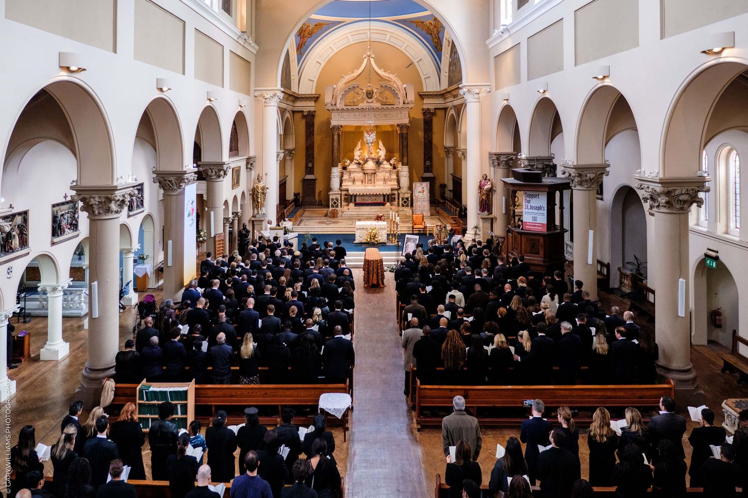Congregation gathered in a traditional church sanctuary with white arched columns and ornate altar during a service.