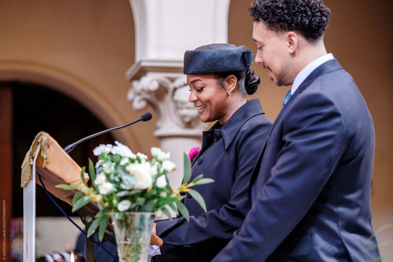 Two people in formal attire share a joyful moment while reading from a book at an elegant venue.