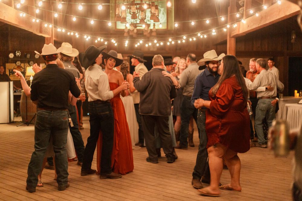 Couples dance together under warm string lights at a rustic barn wedding reception.