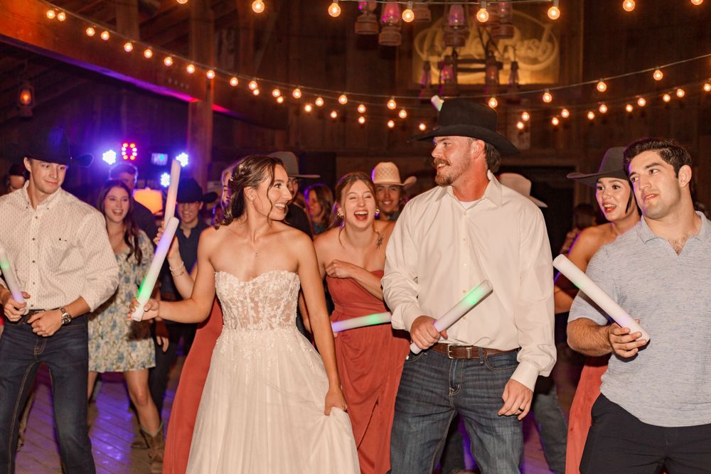 Lively dance floor scene at a barn wedding with string lights and western-themed attire.