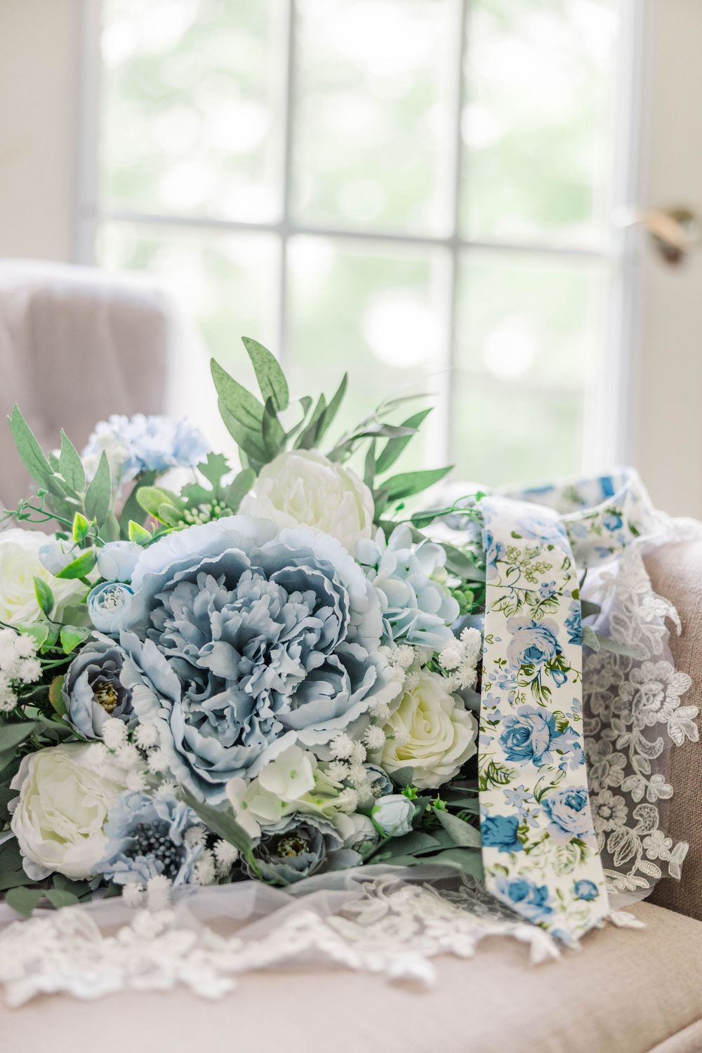 A stunning blue and white wedding bouquet with peonies and roses resting on lace fabric.