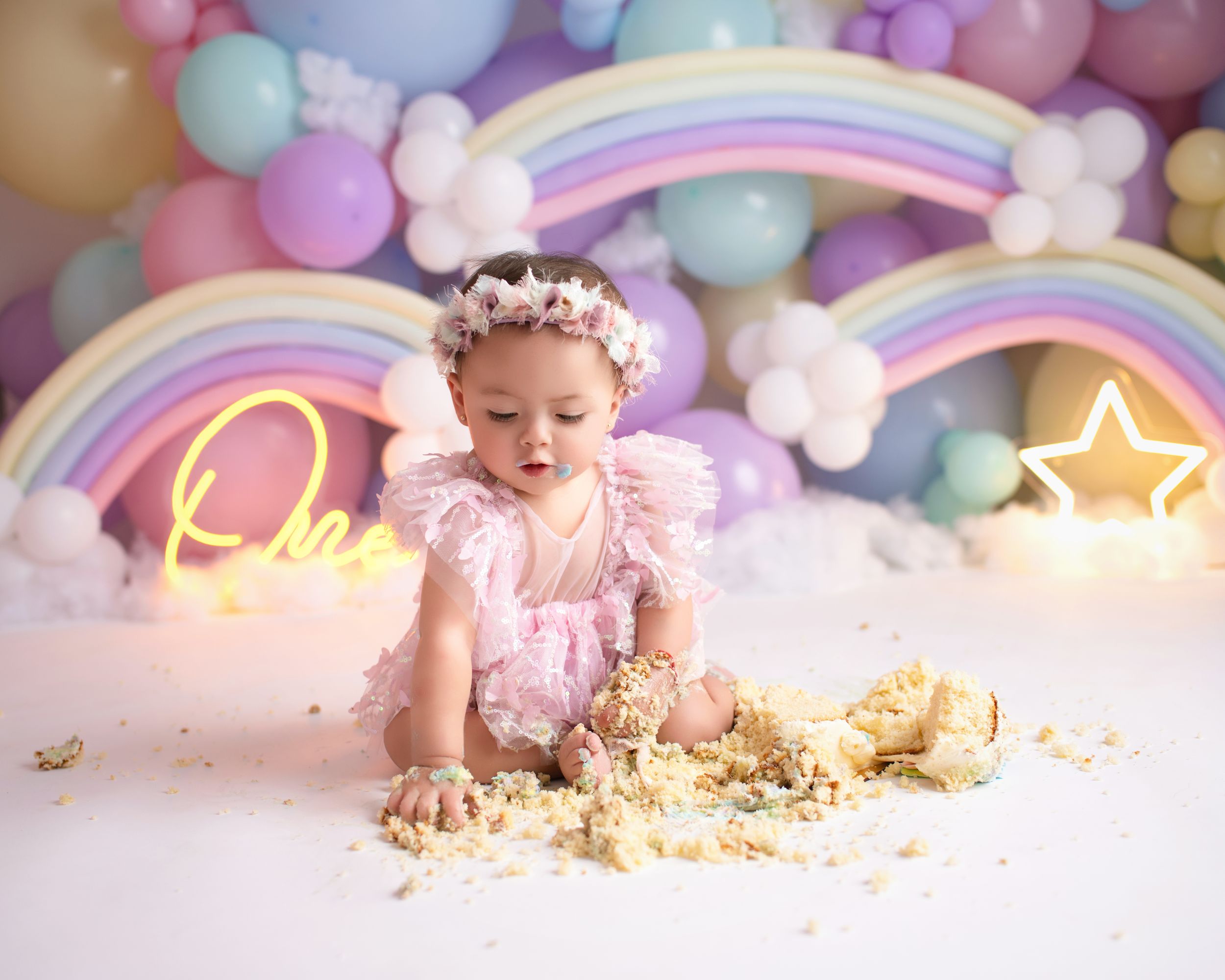 Joyful cake smash photography with rainbow backdrop, neon signs and scattered cake crumbs.