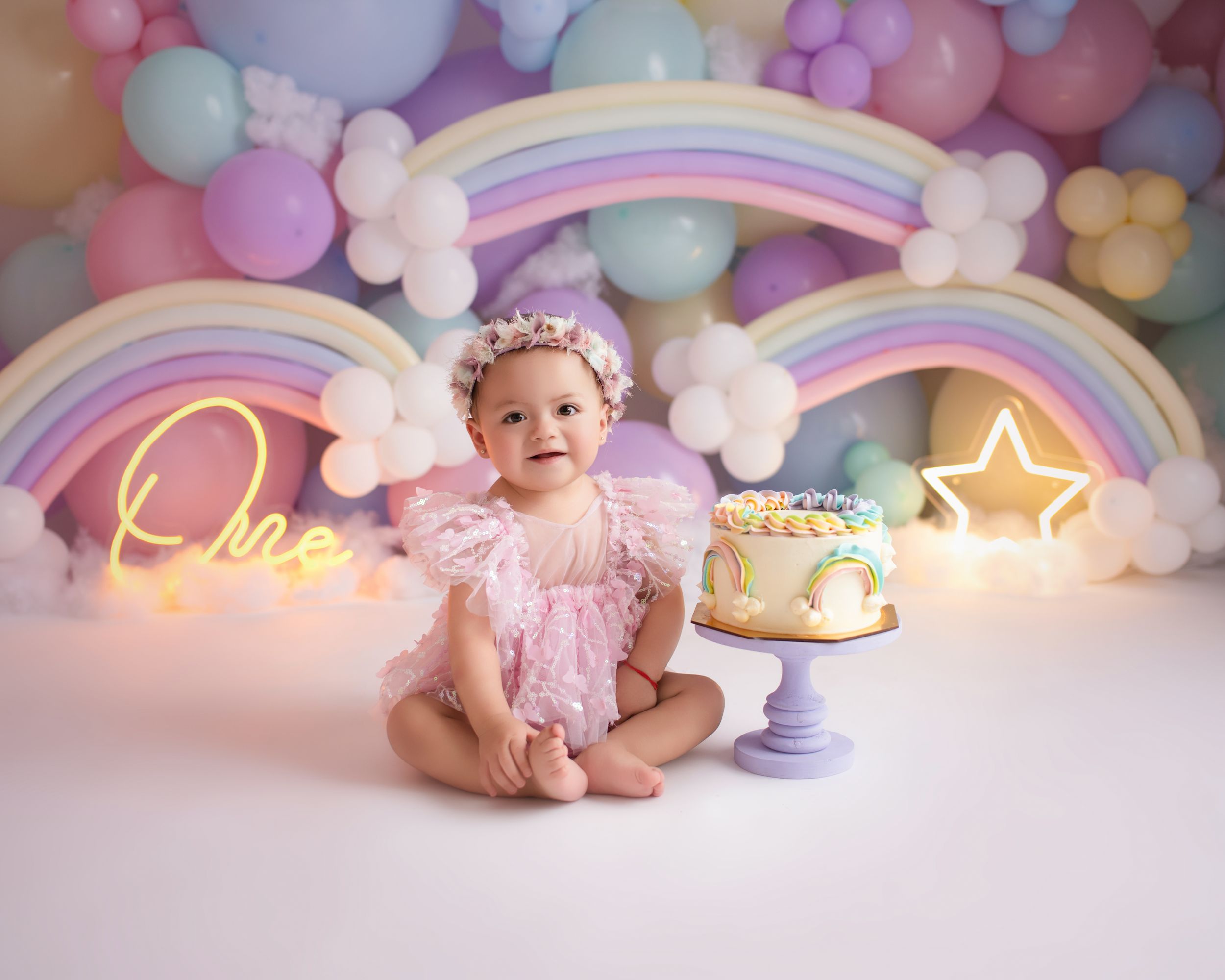 Colorful first birthday scene with rainbow neon lights and pastel balloon arch.