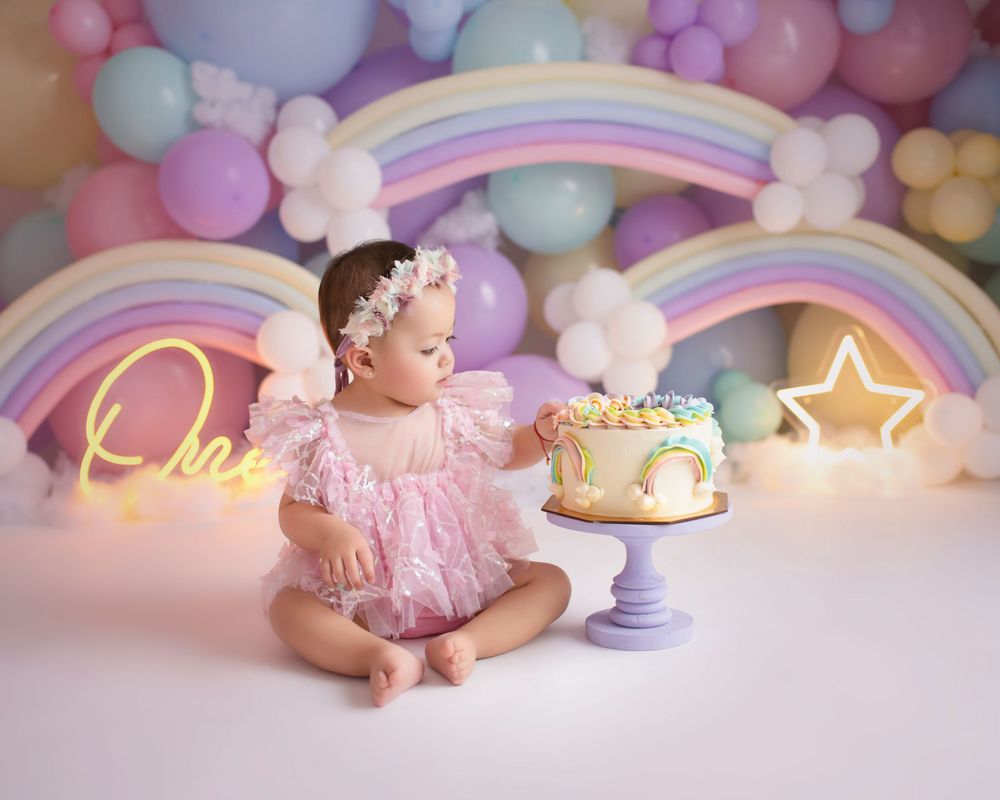 Magical cake smash session with rainbow arches, pastel balloons and glowing neon decorations.