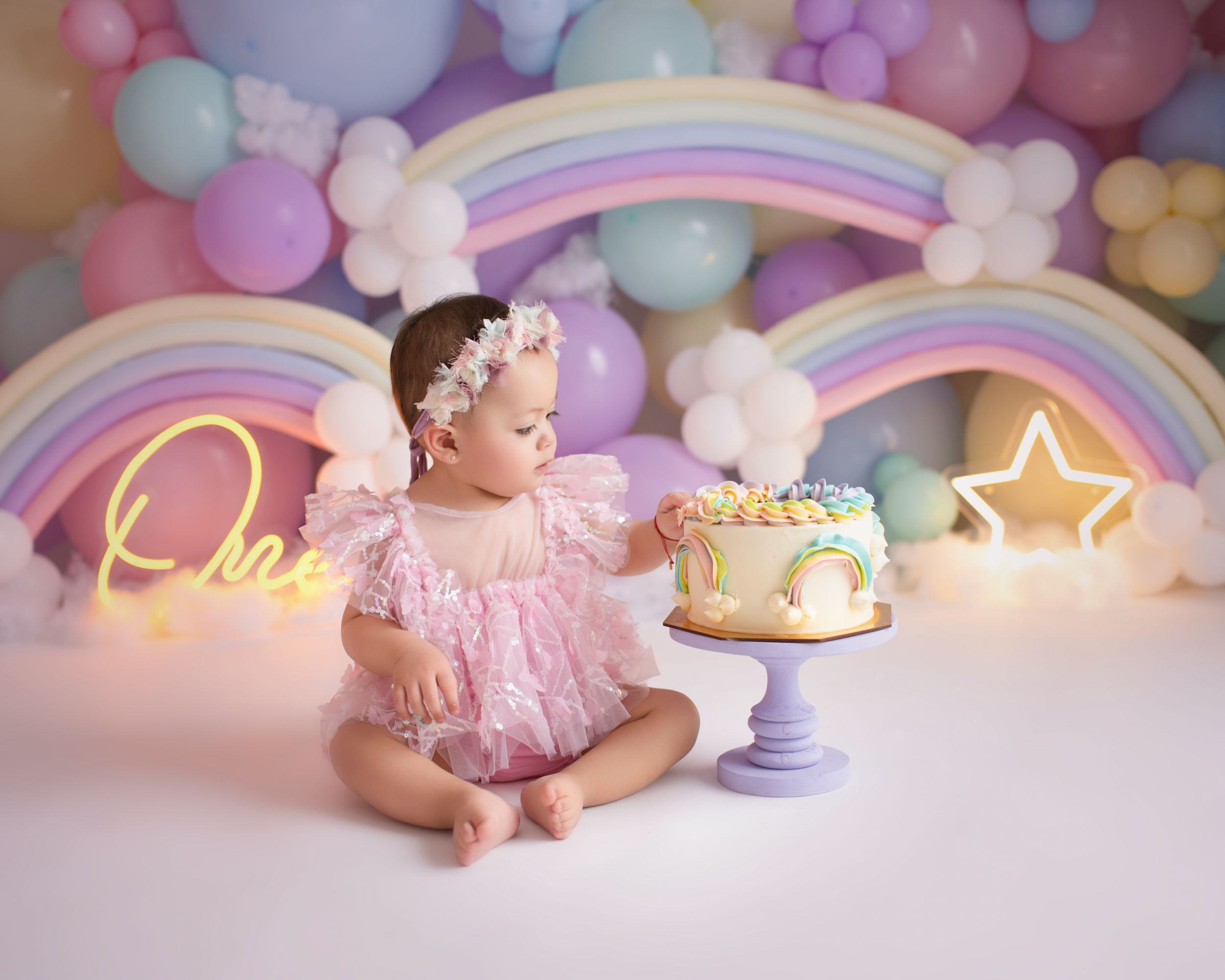 Magical cake smash session with rainbow arches, pastel balloons and glowing neon decorations.