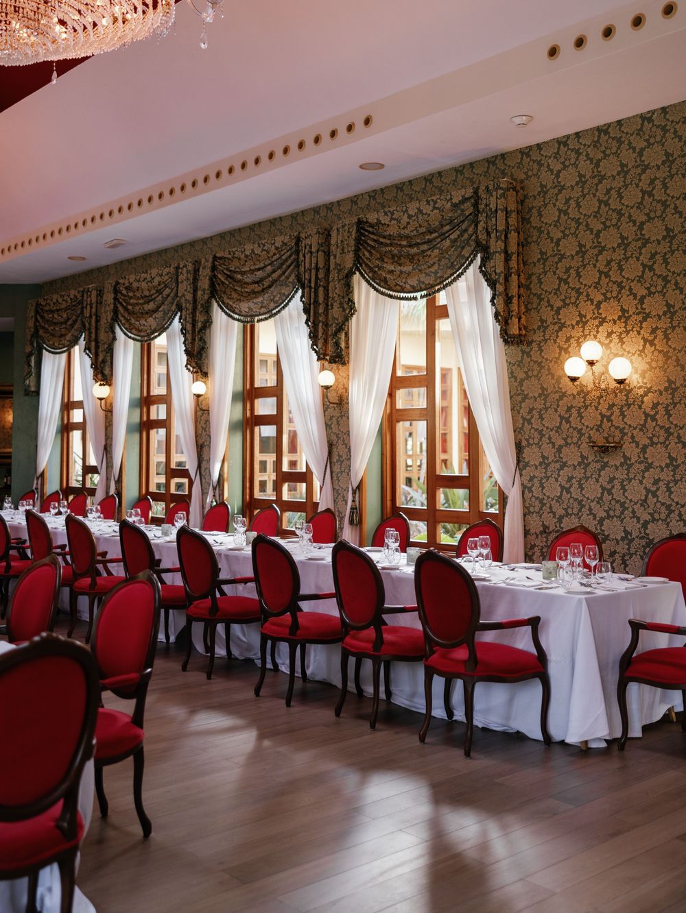 Elegant banquet hall interior with red upholstered chairs, white tablecloths, and ornate wallpaper decor.