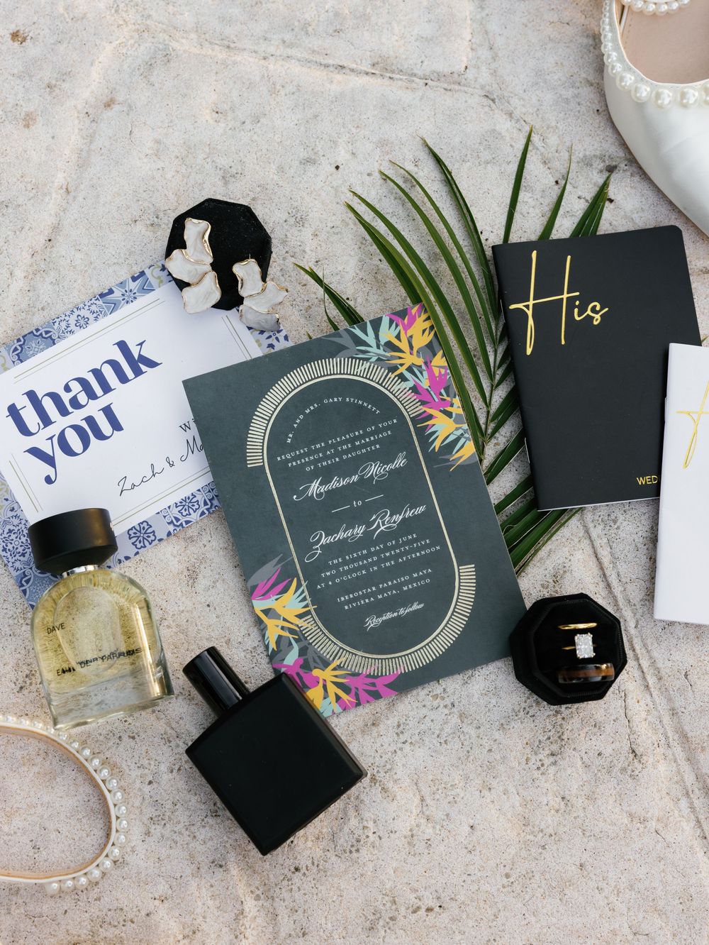 Wedding invitation suite with perfume bottles, palm leaves and elegant stationery on textured surface.