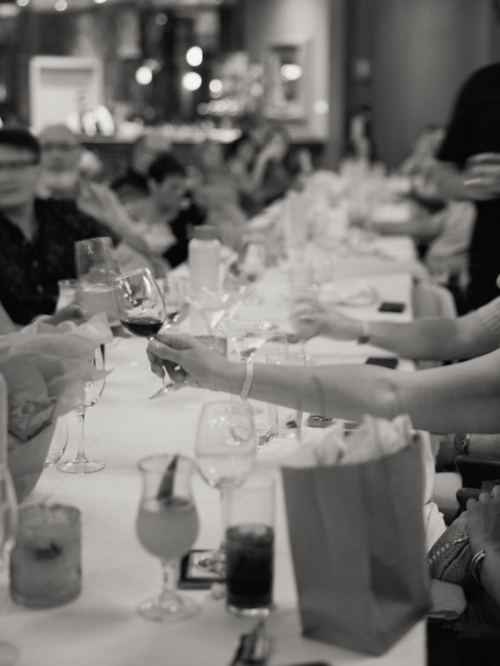 Black and white image of wine glasses being toasted across a formal dining table setting.