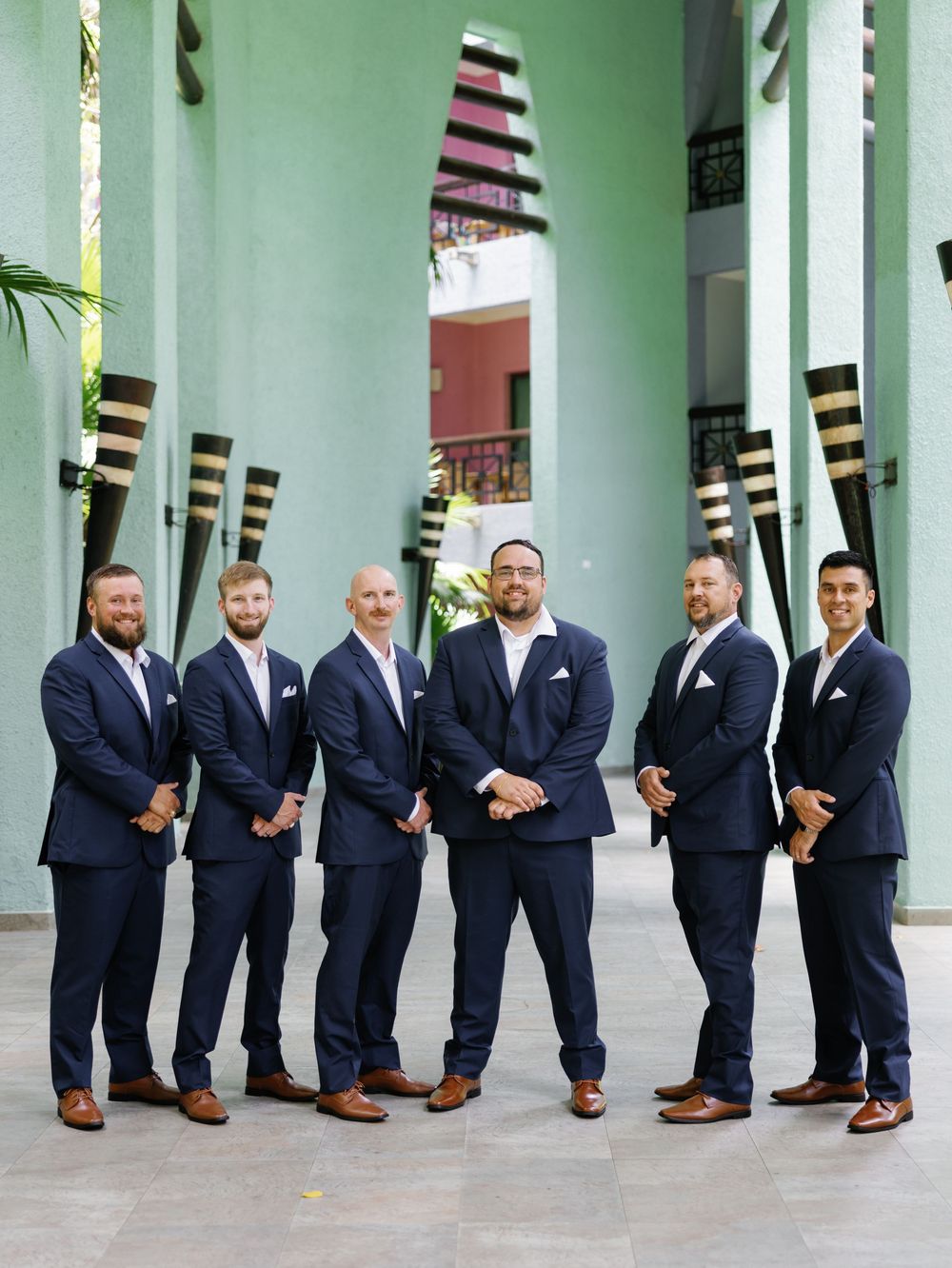 A group of groomsmen in navy suits standing in front of a mint green wall with striped architectural elements.