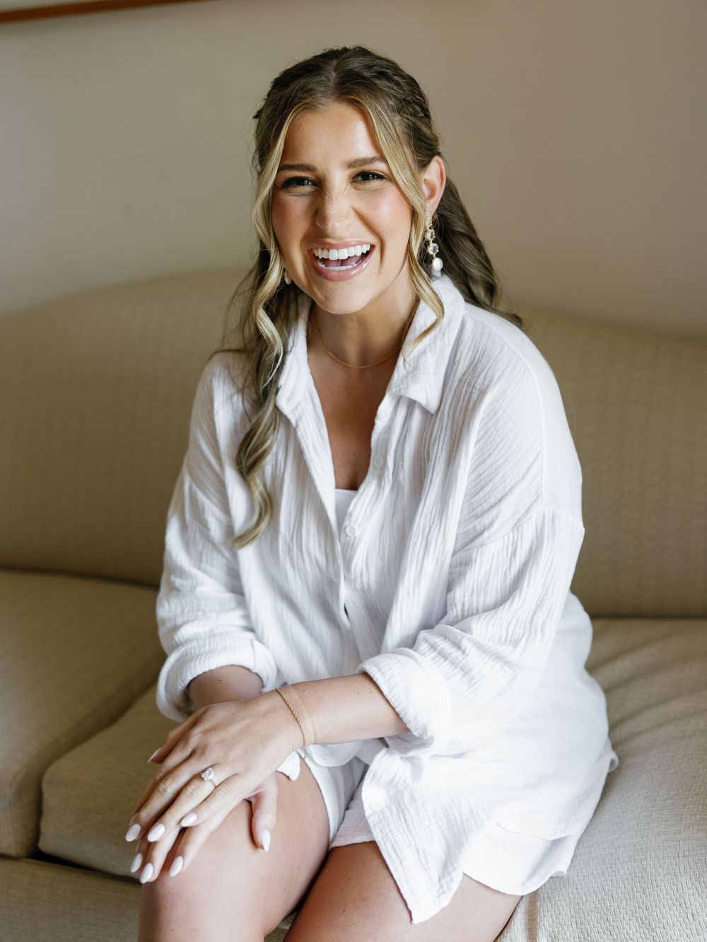 Portrait of someone in a white button-down shirt sitting on a beige couch with a joyful expression.