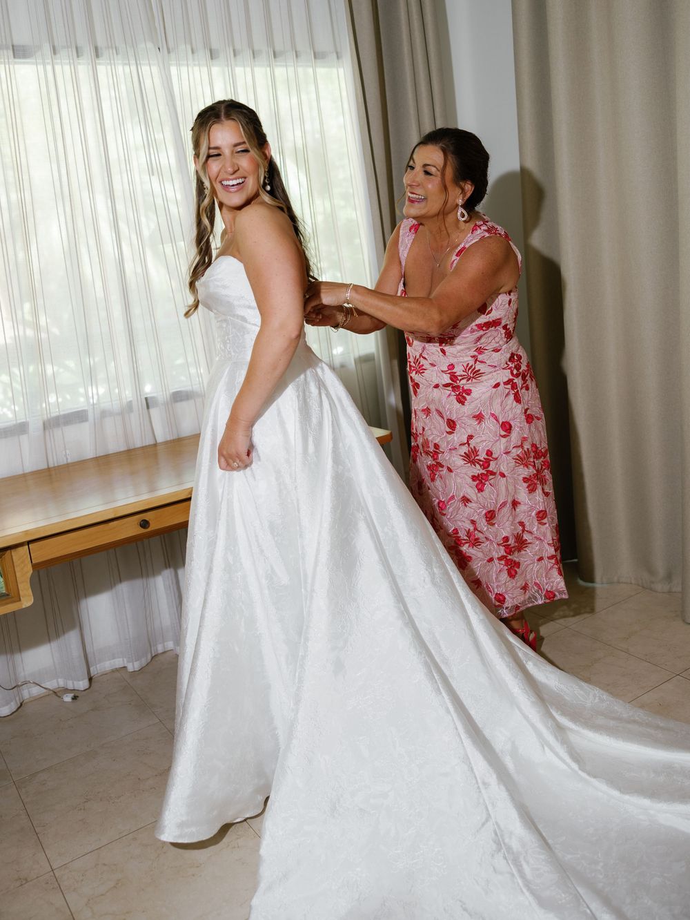 A wedding dress fitting scene showing the final adjustments being made to a beautiful white gown.