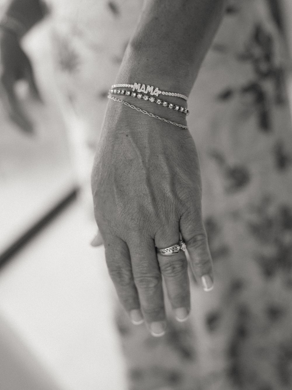 Close-up black and white photo of a hand wearing delicate bracelets and an engagement ring.