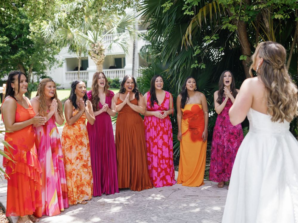 Wedding party in vibrant orange and pink dresses standing with bride in tropical garden setting.