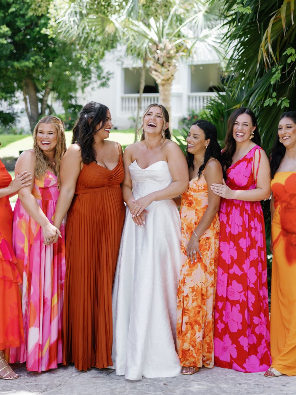Group wearing vibrant orange and pink floral dresses standing together outdoors in a tropical garden setting.