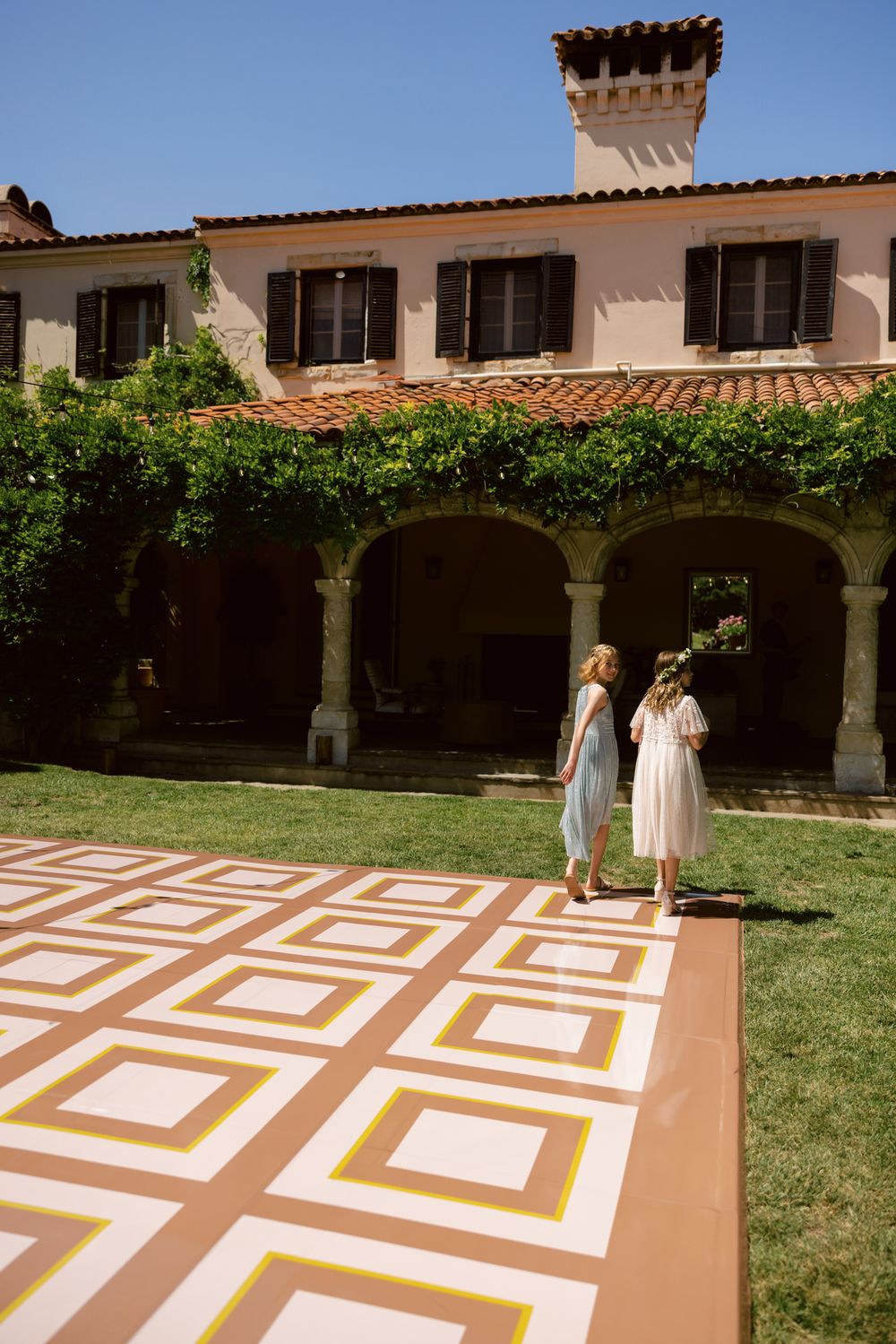 A Spanish-style courtyard with geometric patterns painted on a terracotta patio and arched colonnade.