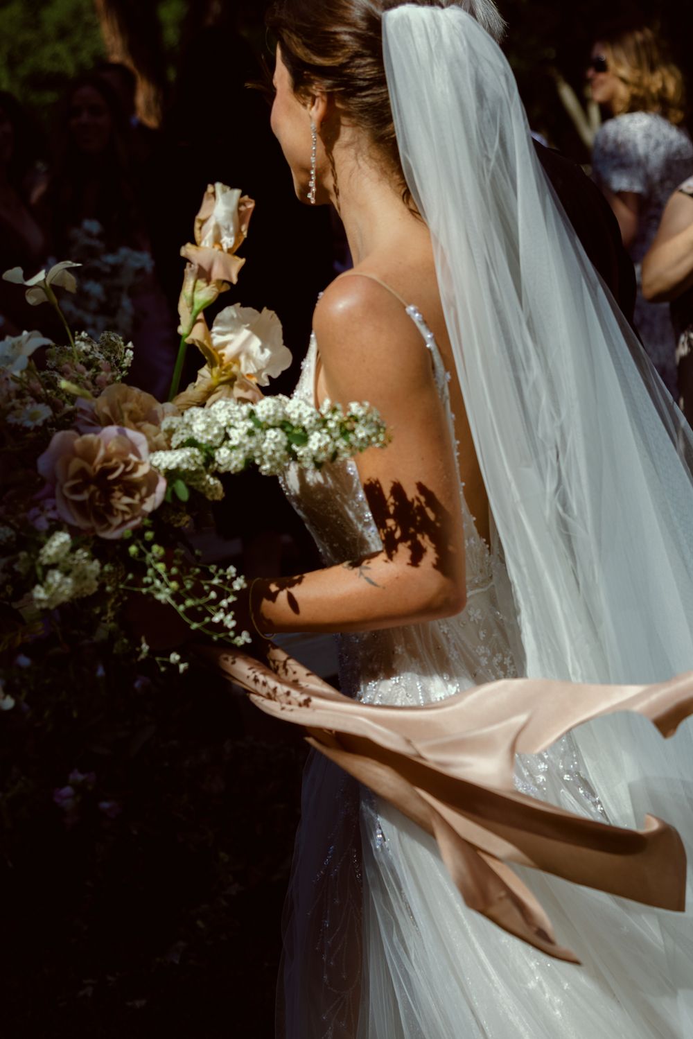 Side view of bride in flowing veil holding delicate white bouquet with roses and baby's breath on wedding day.