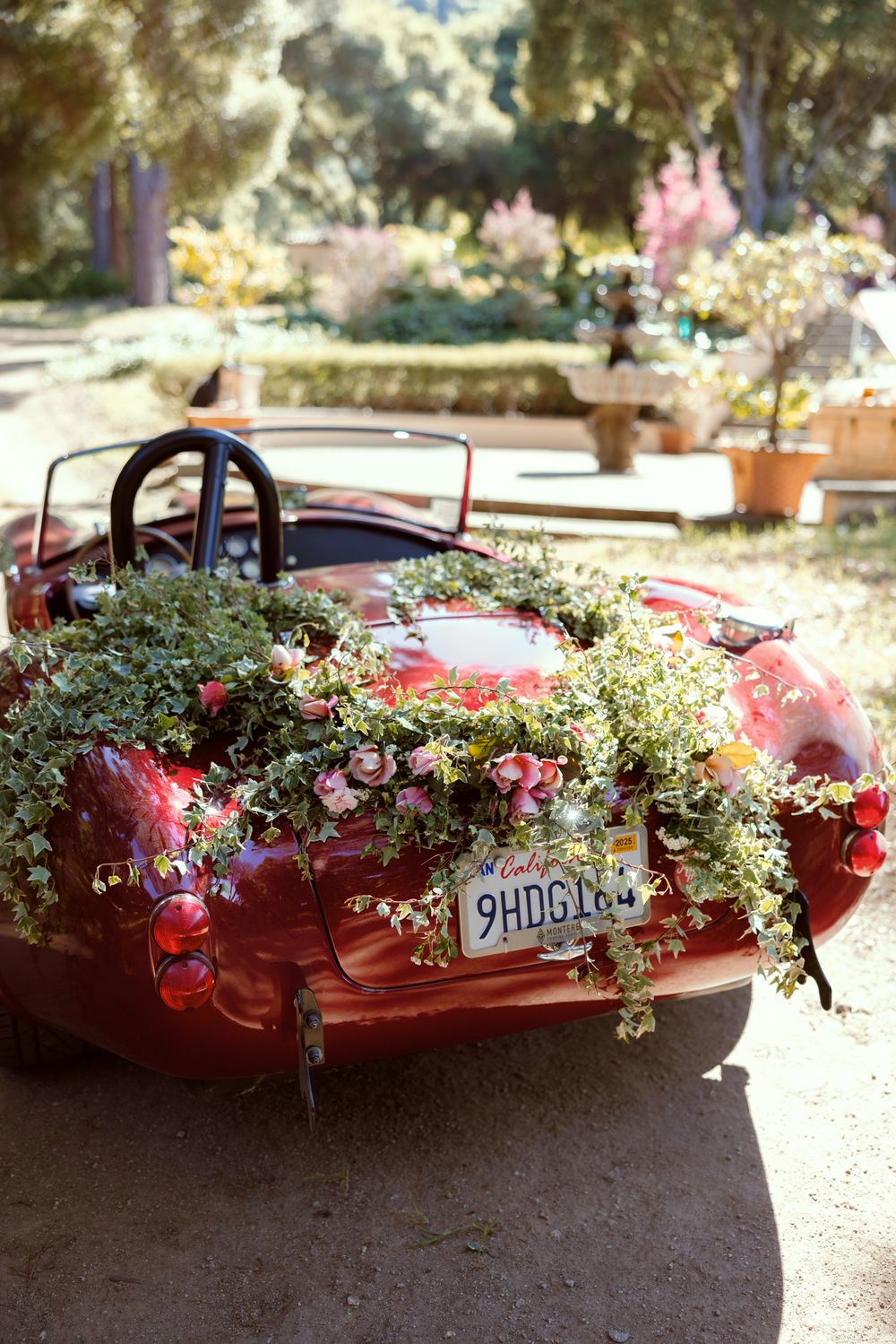 Red vintage convertible car decorated with romantic floral arrangements featuring pink flowers and greenery outdoors.