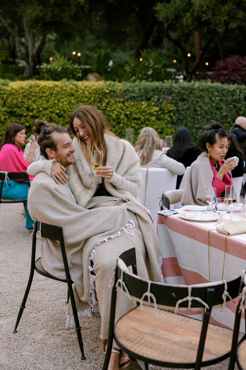 People enjoying an outdoor dinner party at dusk with cozy blankets and table settings in a garden setting.